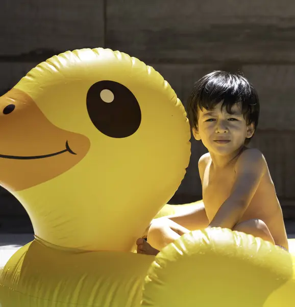 Çocuk havuzda şişme sarı ördekle oynayarak yazın tadını çıkarıyor..