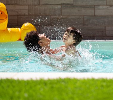 Mutlu bir baba ve oğul güneşli bir yaz gününde birlikte yüzme havuzunda eğleniyor, oynuyor ve su sıçratıyor.