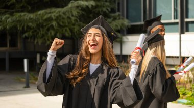 Heyecanlı üniversite öğrencisi mezuniyeti diploma ve arkadaşlarıyla kutluyor.