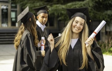 Elinde diplomayla gülümseyen mezun mezuniyetini arkadaşlarıyla kutluyor.