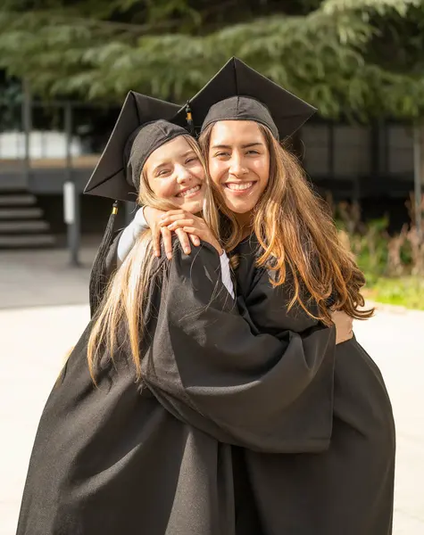 Mezuniyet elbisesi giyen iki kız öğrenci, akademik başarılarını kutluyor.