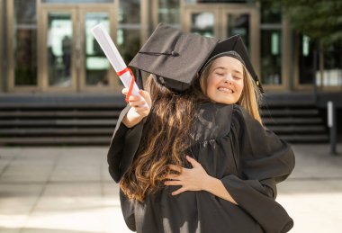 İki bayan mezun birbirine sarılıyor, akademik başarılarını kutluyorlar.