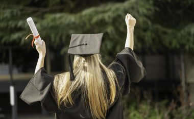 Mezuniyet töreninde diploma ve yumruk kaldıran öğrencinin arka görünüşü