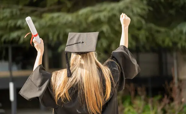 Mezuniyet töreninde diploma ve yumruk kaldıran öğrencinin arka görünüşü