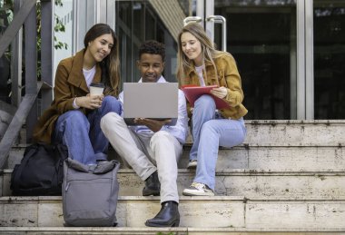 Bir grup öğrenci bir projede birlikte çalışıyorlar. Laptop kullanıyorlar ve dışarıda kahve içiyorlar.