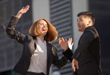 Dışarıda başarıyı kutlayan iki iş ortağı heyecanla ellerini kaldırıyor ve gülümsüyor.
