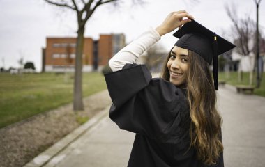Mezuniyet şapkasını düzelten gülümseyen öğrenci kampüste üniversite başarısını kutluyor