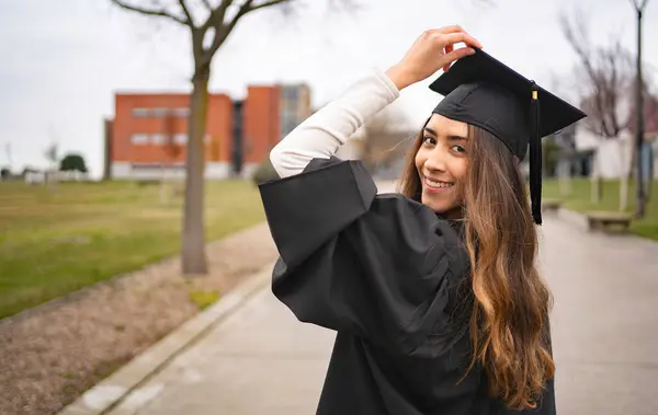 Mezuniyet şapkasını düzelten gülümseyen öğrenci kampüste üniversite başarısını kutluyor