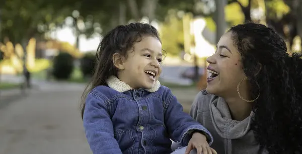 Latin anne ve kızı bir parkta neşe ve kahkaha anı paylaşıyorlar, kaliteli zaman geçiriyorlar.