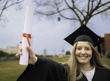 Gülümseyen mezuniyet diploması kırmızı kurdeleyle bağlanmış, mezuniyet elbisesi ve kepi giymiş, akademik başarıyı kutluyor.
