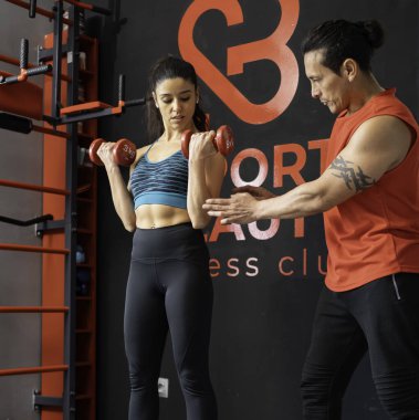 Modern spor salonunda azimli sporcu kadın kişisel antrenörle ağırlık kaldırıyor.