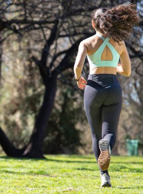 Parkta koşan genç bir sporcunun antrenman rutininin keyfini çıkarırken arka görüntüsü.