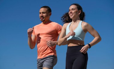 Mavi gökyüzünün altında koşuşturan ırklar arası bir çift sağlıklı yaşam tarzını ve fitness hedeflerini destekliyor..