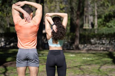 Sportif çift antrenmandan önce parkta kollarını esnetiyor.