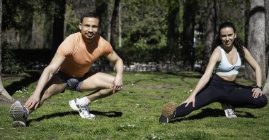 Yeşil parkta koşmadan önce atletik erkek ve kadın ısınıyor ve birlikte bacaklarını açıyorlar.