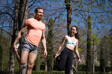 Koşmadan önce parkta bacaklarını esneten, dışarıda egzersiz yapan ırklar arası bir çift..