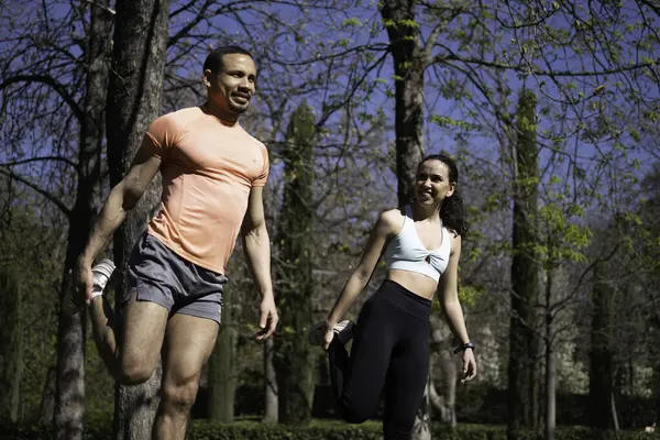 Koşmadan önce parkta bacaklarını esneten, dışarıda egzersiz yapan ırklar arası bir çift..