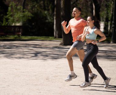 Güneşli bir günde parkta koşan genç çift sağlıklı yaşam tarzını destekliyor.