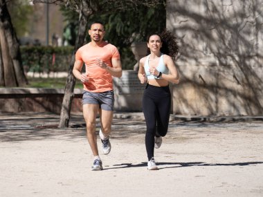 Genç, çok ırklı bir çift parkta spor kıyafetleriyle koşuyor..