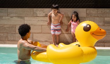 Baba, yaz boyunca oğlu ve kızıyla yüzme havuzunda dev, şişme sarı bir ördekle oynuyor..