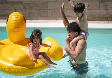 Mutlu İspanyol baba ve çocuklar yüzme havuzunda büyük bir şişme şişeyle oynuyorlar.