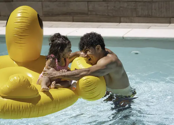 İspanyol baba ve kızı havuzda şişme bir dev üzerinde eğleniyorlar.