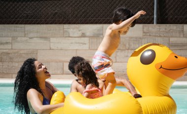 Mutlu Latin ailesi yüzme havuzunda şişme ördekle oynayarak yaz tatilinin tadını çıkarıyor.