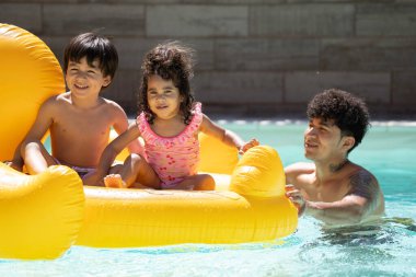 Latin baba şişme ördek itiyor mutlu çocukları yüzme havuzunda taşıyor