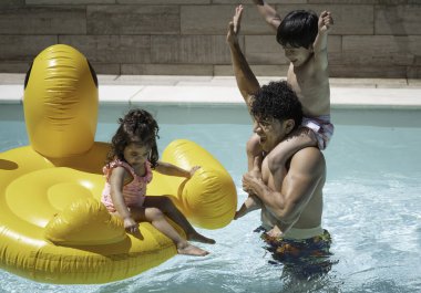 Mutlu İspanyol baba ve çocuklar yüzme havuzunda büyük bir şişme şişeyle oynuyorlar.