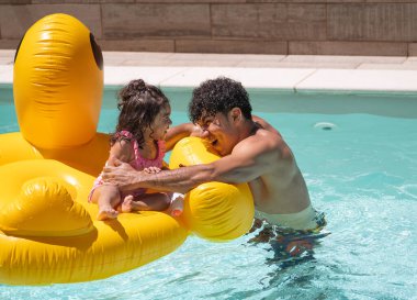 İspanyol baba ve kızı havuzda şişme bir dev üzerinde eğleniyorlar.