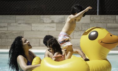 Mutlu Latin ailesi yüzme havuzunda şişme ördekle oynayarak yaz tatilinin tadını çıkarıyor.