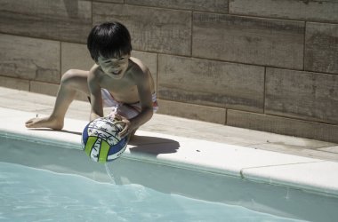 Güneşli bir yaz gününde renkli bir topu yüzme havuzuna atan mutlu Latin çocuk.