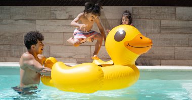 Mutlu Latin ailesi yaz tatilinin tadını çıkarıyor, yüzme havuzunda şişme sarı ördekle oynuyor.