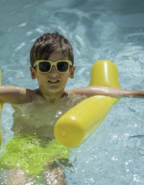 Genç bir çocuk yaz tatilinde sarı şişme kolluklarıyla havuzda rahatlıyor ve eğleniyor.