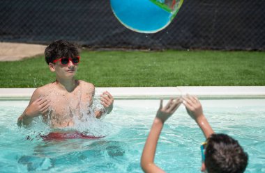 İki genç yaz tatillerinde yüzme havuzunda şişme bir topla oynuyorlar.