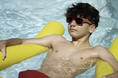 Havuzda sarı şişme bir havuzda güneşli bir günün tadını çıkaran bir çocuk.