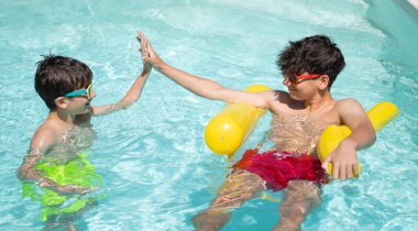 İki mutlu kardeş yaz tatilinde yüzerken ve havuzda oynarken beşlik çakıyor.