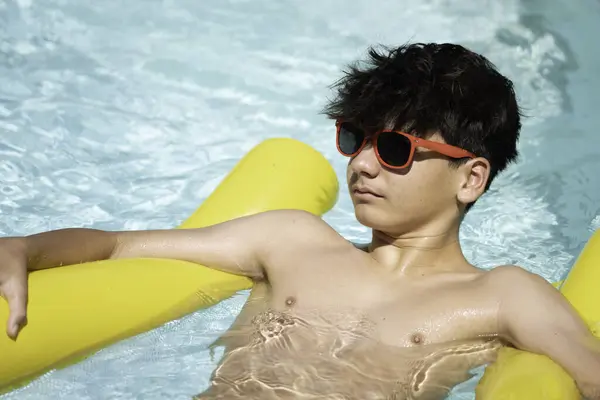 Güneşli bir günün keyfini çıkaran rahat bir gencin yan görüntüsü havuz salında yüzüyor.