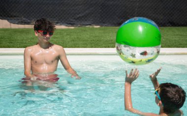 İki arkadaş yaz tatillerinde yüzme havuzunda renkli şişme bir topla oynuyorlar.