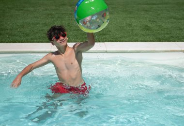 Güneşli bir yaz gününde havuzda fotokopi odasıyla şişme top oynayarak eğlenen genç çocuk.