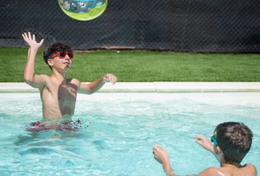 Yaz tatili boyunca yüzme havuzunda şişme topla oynayan iki neşeli genç.