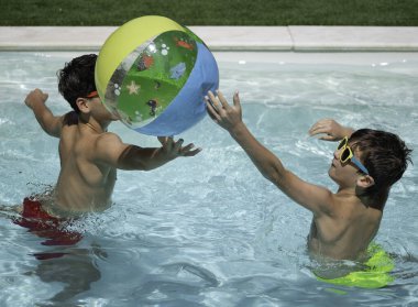 Güneş gözlüğü takan iki çocuk yaz boyunca yüzme havuzunda şişme topla oynuyorlar.
