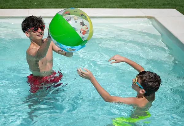 İki genç yaz tatilinin tadını çıkarıyorlar, ferahlatıcı bir yüzme havuzunda renkli şişme bir topla oynuyorlar.