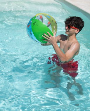 Genç bir adam yaz boyunca ferahlatıcı bir yüzme havuzunda renkli şişme bir topla oynarken eğleniyor.