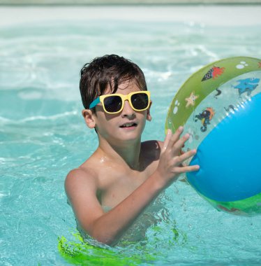 Yazın yüzme havuzunda renkli şişme topla oynayan çocuk portresi.