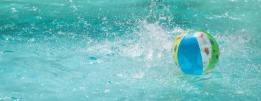 Parlak şişme plaj topu kristal berrak bir yüzme havuzunun yüzeyinde nazikçe sallanarak kopya alanı ile davet edilen turkuaz sularda dalgalanmalar yaratır.