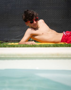 Güneş gözlüklü genç adam güneşli bir günde havuzun kenarında uzanıyor.