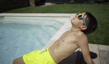Güneş gözlüklü genç çocuk, havuz kenarında fotokopi çekilen güneşli bir günün keyfini çıkarıyor.