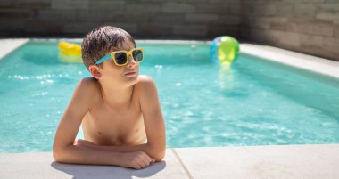 Çocuk renkli oyuncaklarla havuz kenarında güneşli bir günün tadını çıkarıyor.