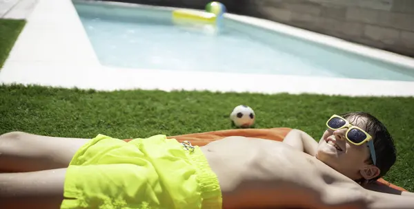 Güneş gözlüklü mutlu çocuk havuz kenarında yazın tadını çıkarıyor.